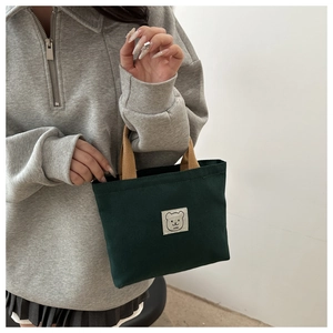 Detail of green canvas tote bag featuring cute bear embroidery and brown ribbon handles
