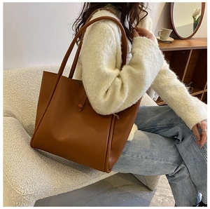Brown leather tote bag styled with white sweater and jeans on a white boucle sofa