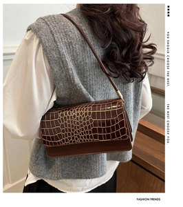 Detailed texture of brown crocodile pattern shoulder bag with gold trim on the flap
