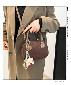 Detail of dark brown suede handbag with plush charm and adjustable strap on a model