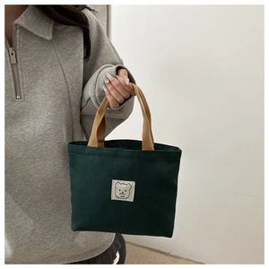 Detail of dark green canvas mini tote bag with cartoon bear patch and khaki handles