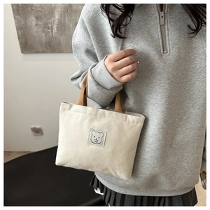 Detail of canvas mini tote bag featuring a cute bear patch and brown handle