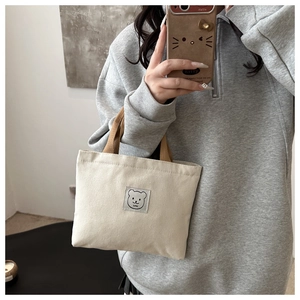 Detailed shot of an off-white canvas tote bag with a cute bear patch and brown handles