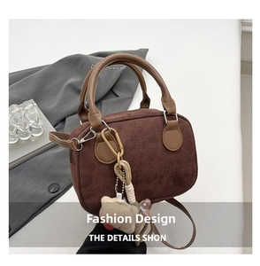 Detail view of brown corduroy bowling bag with plush charm and leather handles