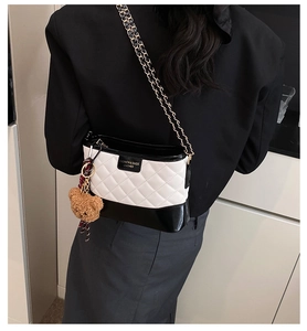Detail of quilted leather crossbody bag with contrast stitching and teddy bear charm