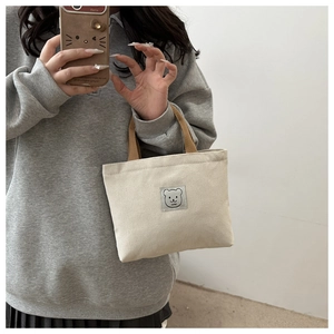 Close-up of canvas bucket bag featuring bear logo patch and brown woven handle detail
