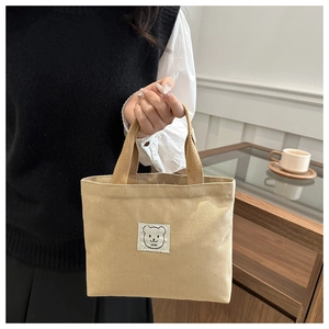 Close-up of a khaki canvas mini tote bag with a cute white bear patch and carry handle