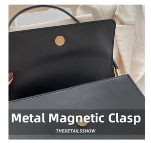 Close-up of black textured leather handbag featuring a golden circular magnetic snap closure