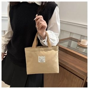 Close-up of beige canvas tote bag with cute bear patch and handle held by a model