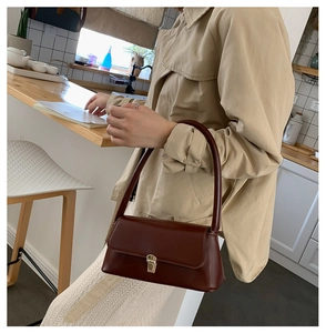 Détail du sac baguette marron foncé en similicuir brillant avec fermoir doré chic