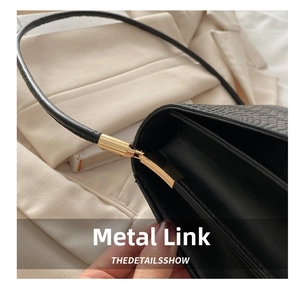 Detail of black animal-textured leather bag with shiny gold metal ring and strap connector