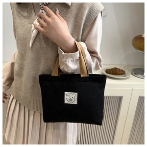 Detailed view of black canvas bucket bag with brown handles and a cute cartoon bear patch
