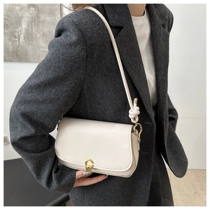 Detail of cream saddle bag with golden clasp worn over a grey tweed blazer