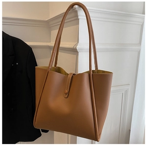 Detail of brown leather tote bag with sturdy stitching and shoulder strap on a white wall