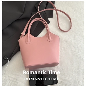 Pink minimalist leather bucket bag with top handles and adjustable strap next to a phone