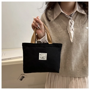 Detailed view of black canvas tote bag with cute bear patch and brown handles