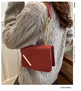 Détail du sac bandoulière rouge tressé avec chaîne dorée et garniture métallique