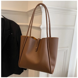 Detail of deep brown tote bag hanging on a white wall next to a black blazer jacket