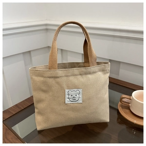 Detailed close-up of a minimalist khaki canvas bag with a cute bear logo on a glass table