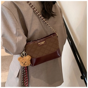 Detail of rhombic stitched shoulder bag with chain strap and plush bear pendant