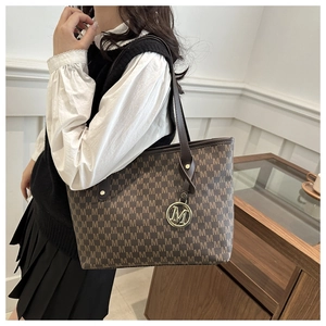 Detail of a brown leather tote bag featuring monogram M print and a round metallic pendant