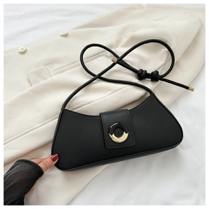 Detail of a black leather baguette bag featuring a gold buckle on a beige blazer