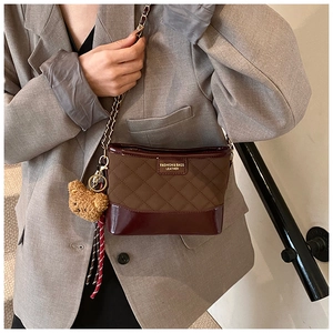 Detail of rhombic quilted crossbody bag in brown and burgundy with gold chain and bear charm