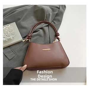 Close-up of elegant dark coffee shoulder bag with golden metal bar and knot handle detail