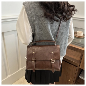 Detailed view of dark brown faux leather crossbody bag with buckle straps and top handle