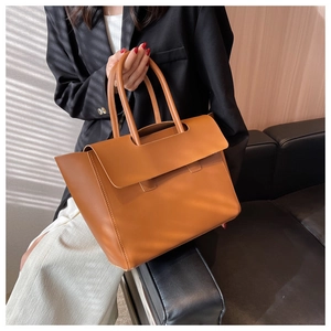 Macro detail of camel brown leather tote bag with unique flap closure and dual handles