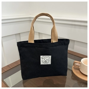 Detail of cute bear patch and woven handles on a minimalist black canvas tote bag