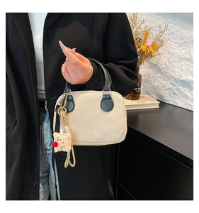 Detail of off-white textured handbag with black leather handle and plush charm