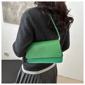 Detail of green baguette shoulder bag featuring a woven flap and metallic buckle