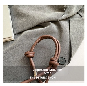 Detail of a brown leather adjustable shoulder strap with knot on grey blazer fabric