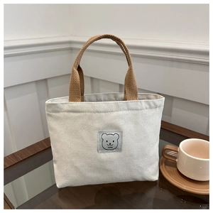 Close-up of canvas handbag with brown woven handles and cute bear patch detail