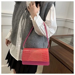 Sac baguette rose à motif crocodile et boucles métalliques porté par un mannequin