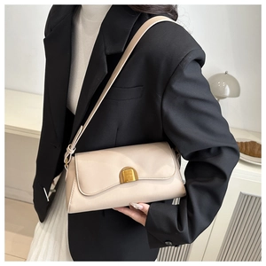 Détail du sac baguette crème avec boucle dorée porté sur un blazer noir élégant