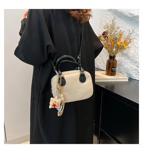 Detail of beige fleece crossbody pillow bag with black leather straps and biscuit charm
