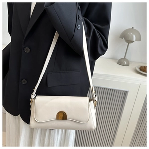Détail d'un sac porté épaule crème avec boucle dorée et surpiqûres sur un blazer noir