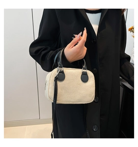 Detail of matte cream bowling bag with black leather handles and embossed 2DI logo