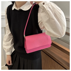 Close-up of bright pink shoulder bag with crocodile texture worn by model