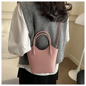 Pink bucket bag worn by model featuring circular handles and gold hardware details