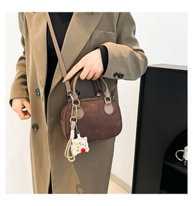 Brown suede crossbody bag detail featuring a white teddy bear charm and sleek top handle