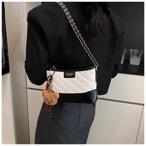 Detail of crossbody bag featuring quilted patterns, metal chain strap and plush bear charm