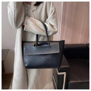 Detail of minimalist black leather tote bag showing textured stitching and hollow handles