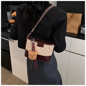 Detail of rhombic quilted crossbody bag in beige and burgundy with plush bear charm