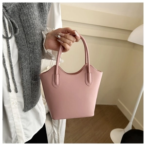 Detail of light pink PU leather bucket bag held by model wearing a white shirt and vest