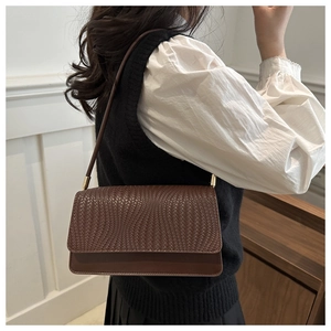 Detail of dark brown baguette bag featuring woven texture and smooth leather finish