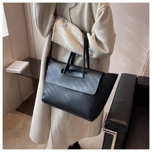 Detail of minimalist black leather tote bag with geometric cutout handle held by model