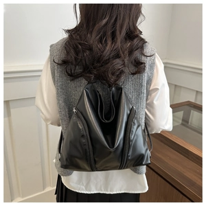 Detail of a black leather backpack featuring a unique triangular fold and silver side zippers